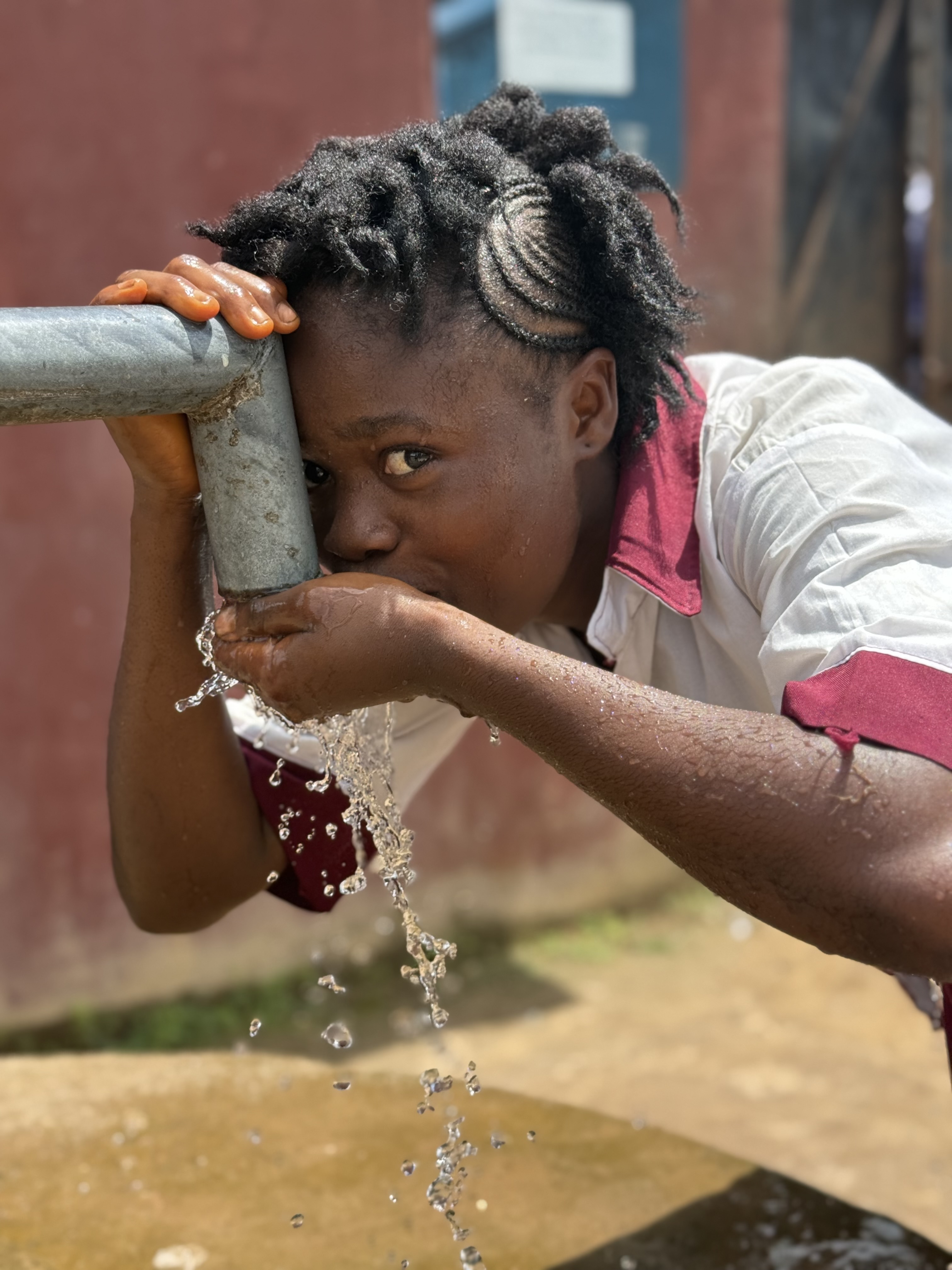 Een meisje drinkt schoon water rechtstreeks uit de pomp